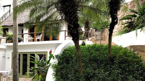 A white building with a curved roof, surrounded by lush greenery including palm trees and various plants. - Mi Media Naranja-Ocean view luxury casita (San Pancho)