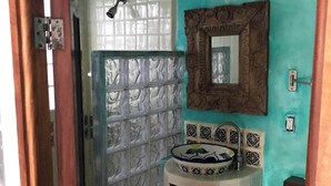 A bathroom with a turquoise wall, a glass shower enclosure, a white sink with a decorative bowl, and a mirror with a wooden frame. - Mi Media Naranja-Ocean view luxury casita (San Pancho)