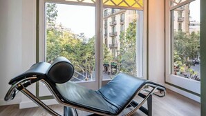 A modern lounge chair with a metal frame and black cushions, positioned in a room with large windows offering a view of a cityscape and greenery.