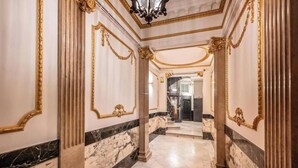 A grand hallway with marble floors, ornate gold detailing, and classical columns.