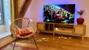 A living room with a television on a wooden stand, a wicker chair, and a red vase on the stand. - T2 "Mediterranean" apartment in the center of Narbonne (Narbonne)