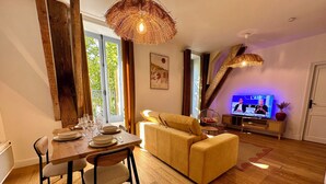 A dining area with a wooden table set for four, a sofa, and a television displaying a news program. - T2 "Mediterranean" apartment in the center of Narbonne (Narbonne)
