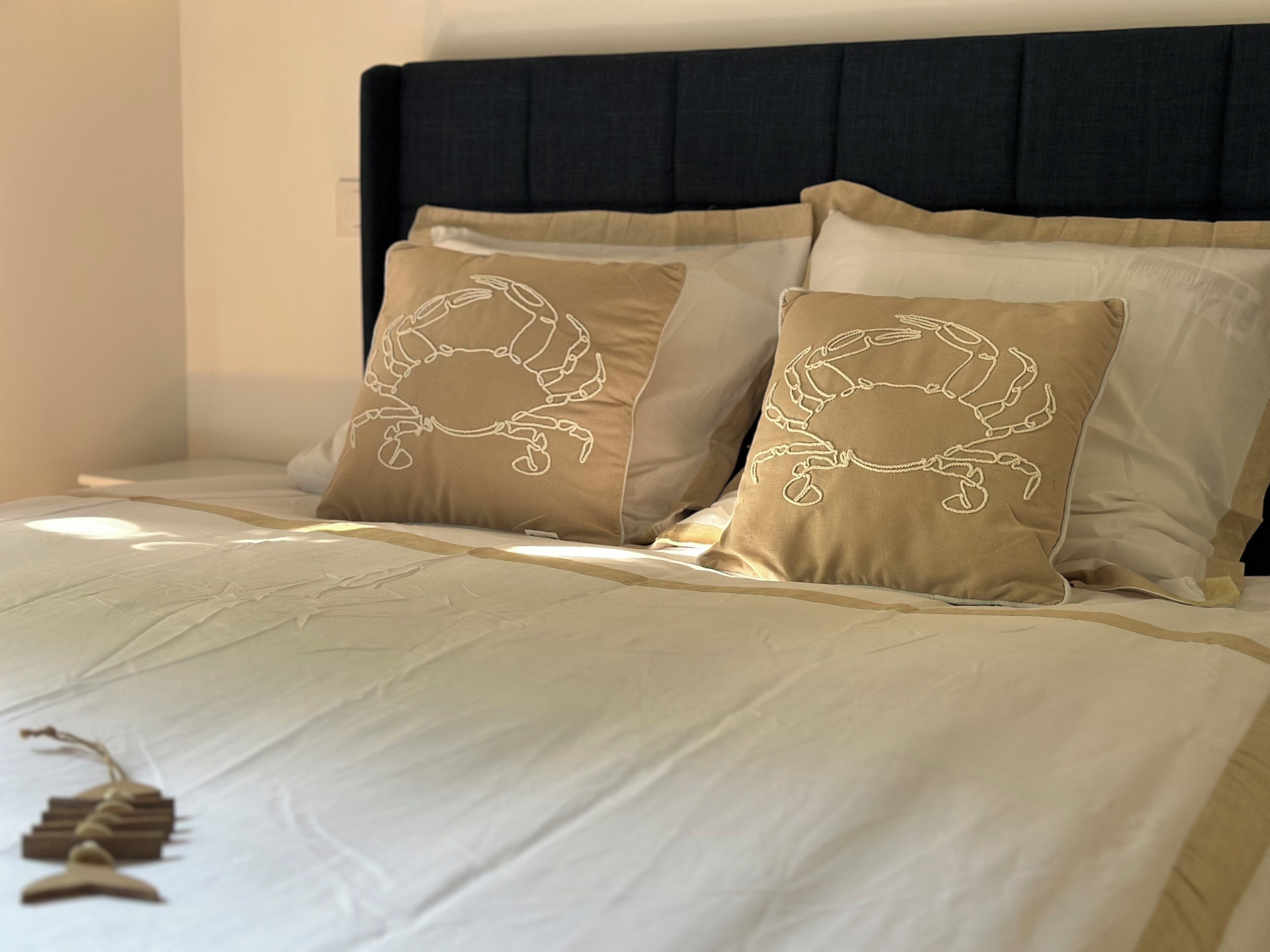 Una cama con cabecera oscura y almohadas color crema con diseño de cangrejo.