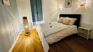 A bedroom with a bed, bedside tables, a lamp, a window with curtains, and wall-mounted lights. - T2 "Mediterranean" apartment in the center of Narbonne (Narbonne)