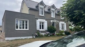 Een tweelaags huis met een grijze gevel en witte omlijsting, met een voortuin en een kleine tafel en stoelen.