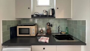 Een kleine keuken met een magnetron, broodrooster, waterkoker en een klein raam boven het aanrecht.