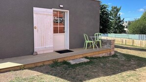 Een gebouw met een houten terras, een deur met een raam en twee groene stoelen buiten.