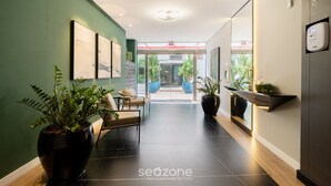 A modern hotel lobby with a green wall, a seating area, and a reception desk.