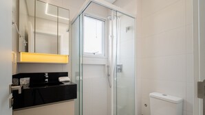 A modern bathroom with a glass-enclosed shower, a black countertop, and a white toilet.