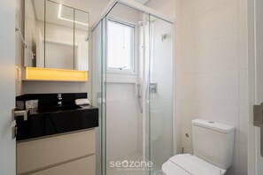 Un baño moderno con ducha de vidrio, encimera negra y retrete blanco.