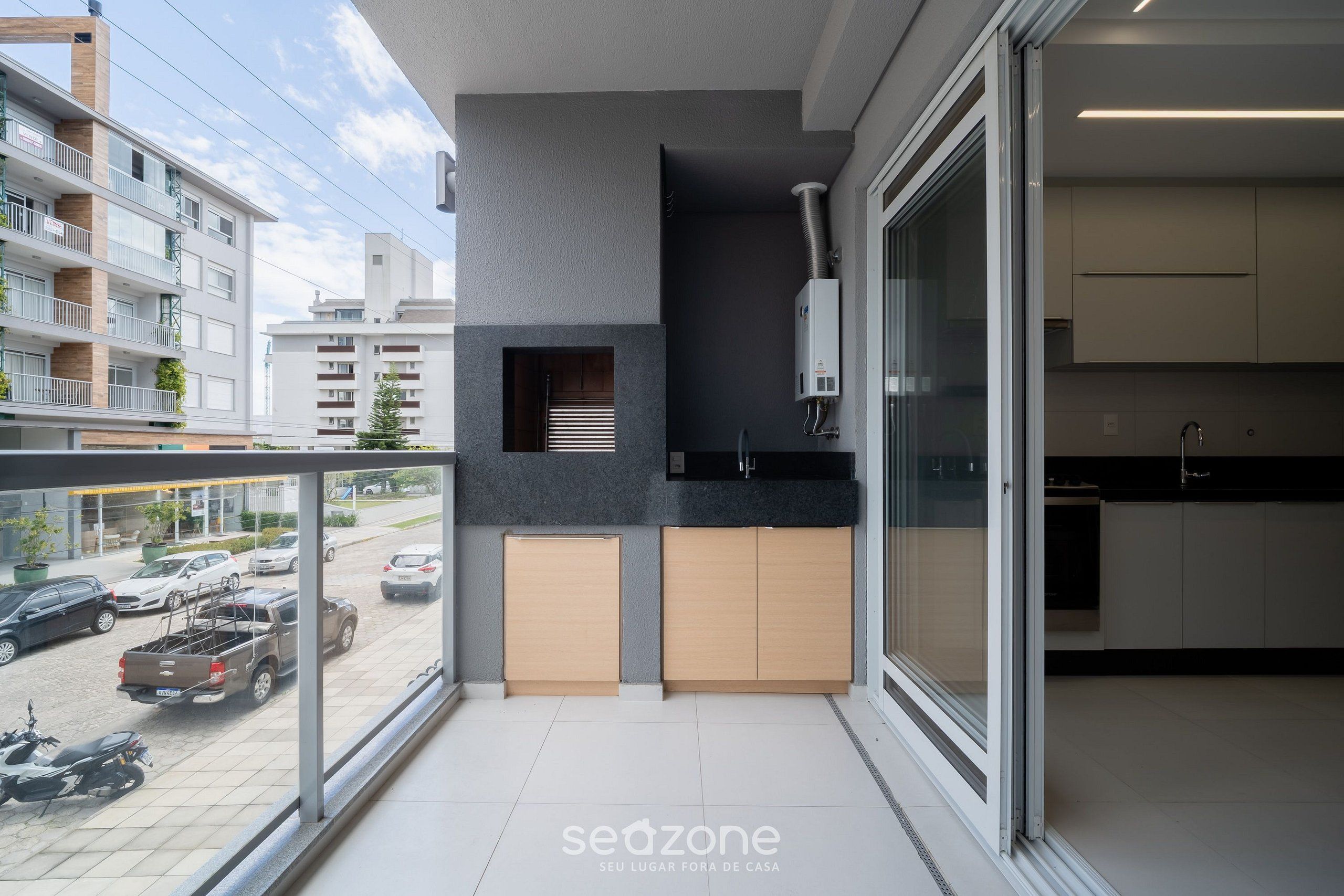 A modern apartment with a balcony, a kitchen with dark countertops, and a view of the street.
