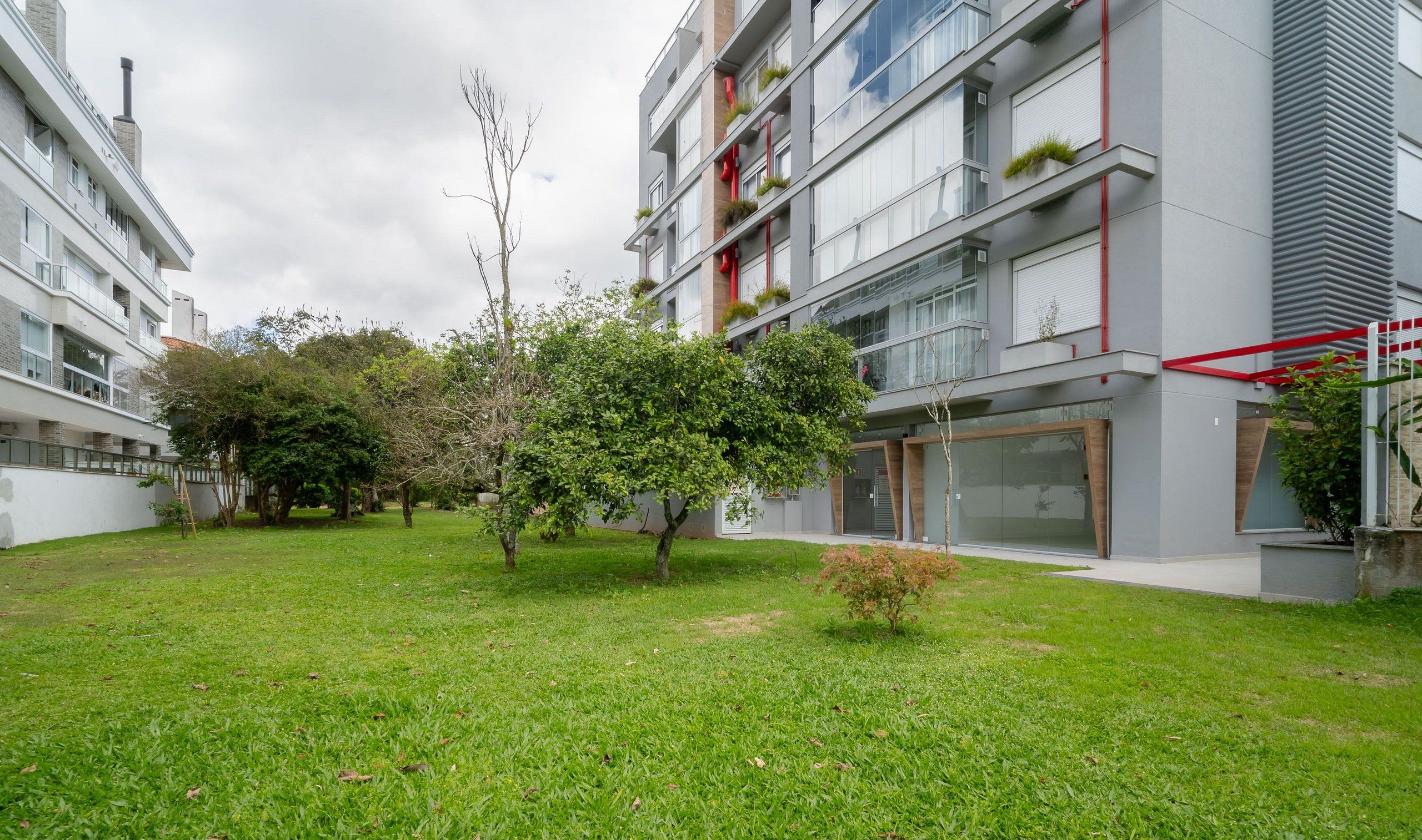 Un moderno edificio de apartamentos con balcones, un patio con césped y árboles.