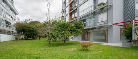 A modern apartment building with balconies, a grassy courtyard, and trees.