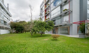 A modern apartment building with balconies, a grassy courtyard, and trees.