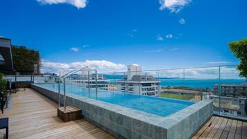 A rooftop infinity pool with a clear view of the ocean and distant mountains.