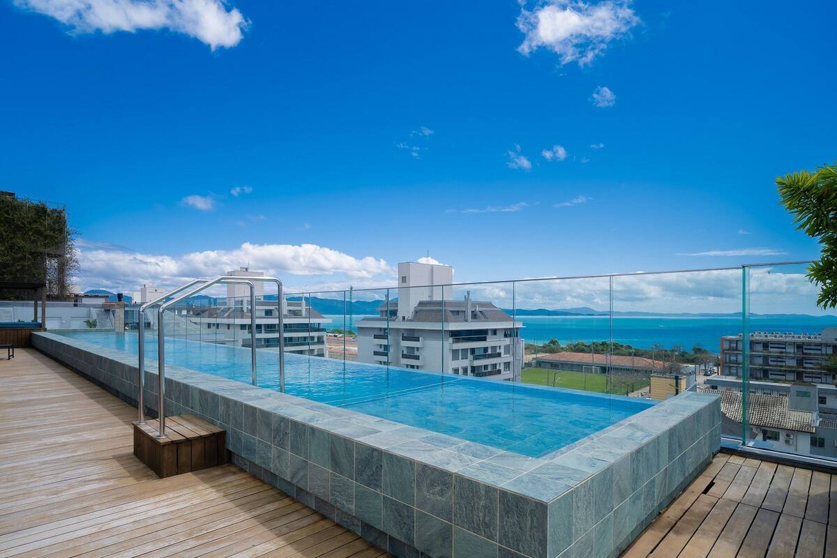 A rooftop infinity pool with a clear view of the ocean and distant mountains.