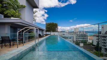 A rooftop infinity pool with a clear view of the cityscape and mountains in the distance.
