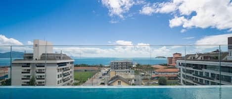A hotel with a pool overlooking a coastal area, featuring a clear sky and distant mountains.