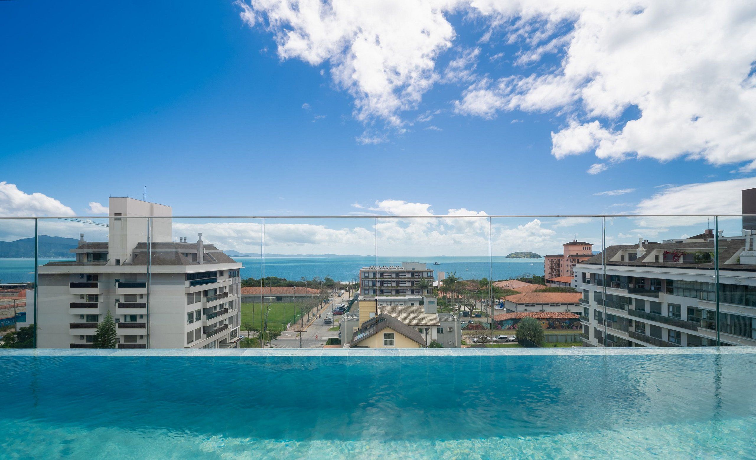 A hotel with a pool overlooking a coastal area, featuring a clear sky and distant mountains.