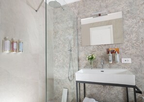 Een badkamer met een douche, wastafel, spiegel en toiletartikelen aan de muur.