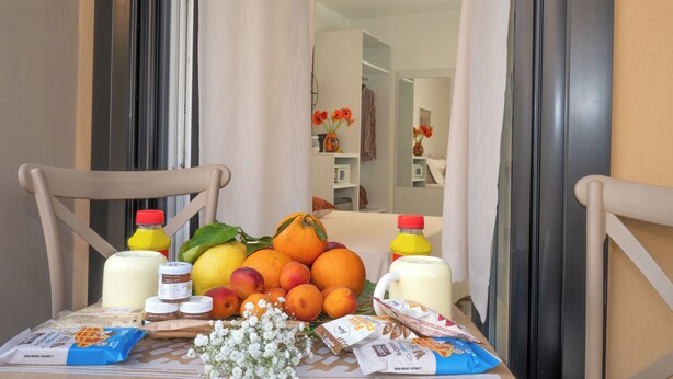 Een ontbijttafel met fruit, toevoegingen en verpakte producten, in een kamer met uitzicht op een gang en een deur.