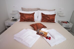 Een netjes opgemaakt bed met witte lakens, twee bruine kussens, een opgevouwen handdoek, een boek getiteld 'POMPEI' en een rode roos.