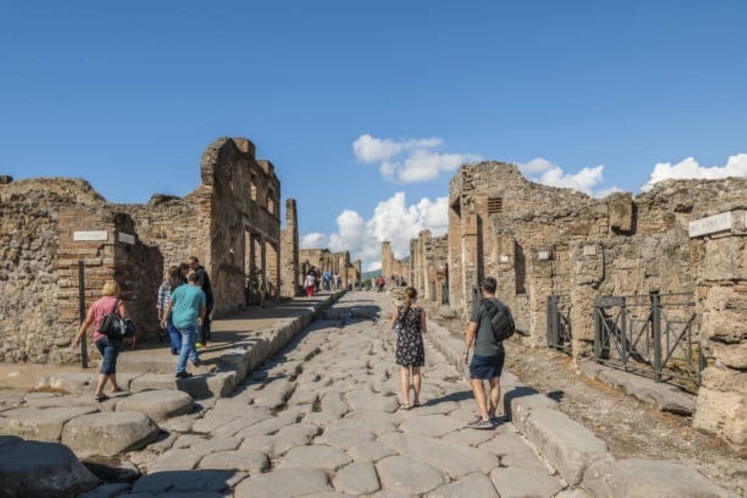 An ancient stone pathway with ruins on either side, leading to a distant structure.
