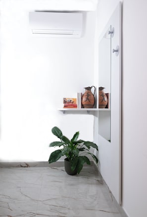Un baño con pared blanca, una planta en maceta, un estante con libros y jarrones, y piso de mármol.