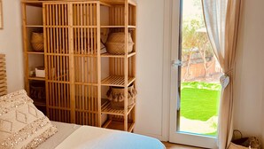 A room with a bed, a wooden shelf with baskets, and a door leading to a green outdoor area. - Japandi Suites, house with garden. Oasis of relaxation 5' from the sea and the airport (Olbia)