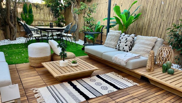 A cozy outdoor seating area with a sofa, ottomans, and a coffee table, surrounded by lush greenery and a bamboo fence. - Japandi Suites, house with garden. Oasis of relaxation 5' from the sea and the airport (Olbia)
