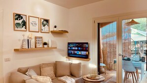 A living room with a sofa, a TV mounted on the wall, and framed pictures. - Japandi Suites, house with garden. Oasis of relaxation 5' from the sea and the airport (Olbia)