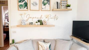 A living room with a sofa, a television, and wall decorations including framed prints and a sign.