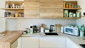 A modern kitchen with wooden cabinetry, a built-in microwave, and various kitchen appliances. - Japandi Suites, house with garden. Oasis of relaxation 5' from the sea and the airport (Olbia)