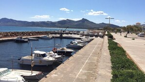 Un puerto deportivo con barcos amarrados, un paseo marítimo pavimentado y montañas al fondo.