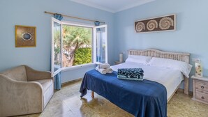 Un dormitorio con una cama, una silla, un ventanal y una pared con un plato decorativo.