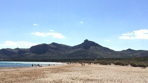Una playa con montañas al fondo y gente en la arena.