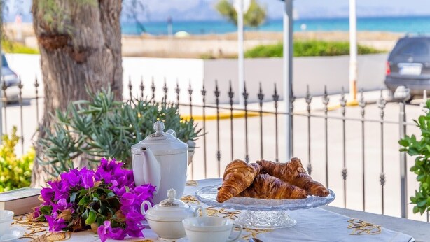 Una mesa con cruasanes, un rincón para té y una taza, frente a un árbol y vista al mar.