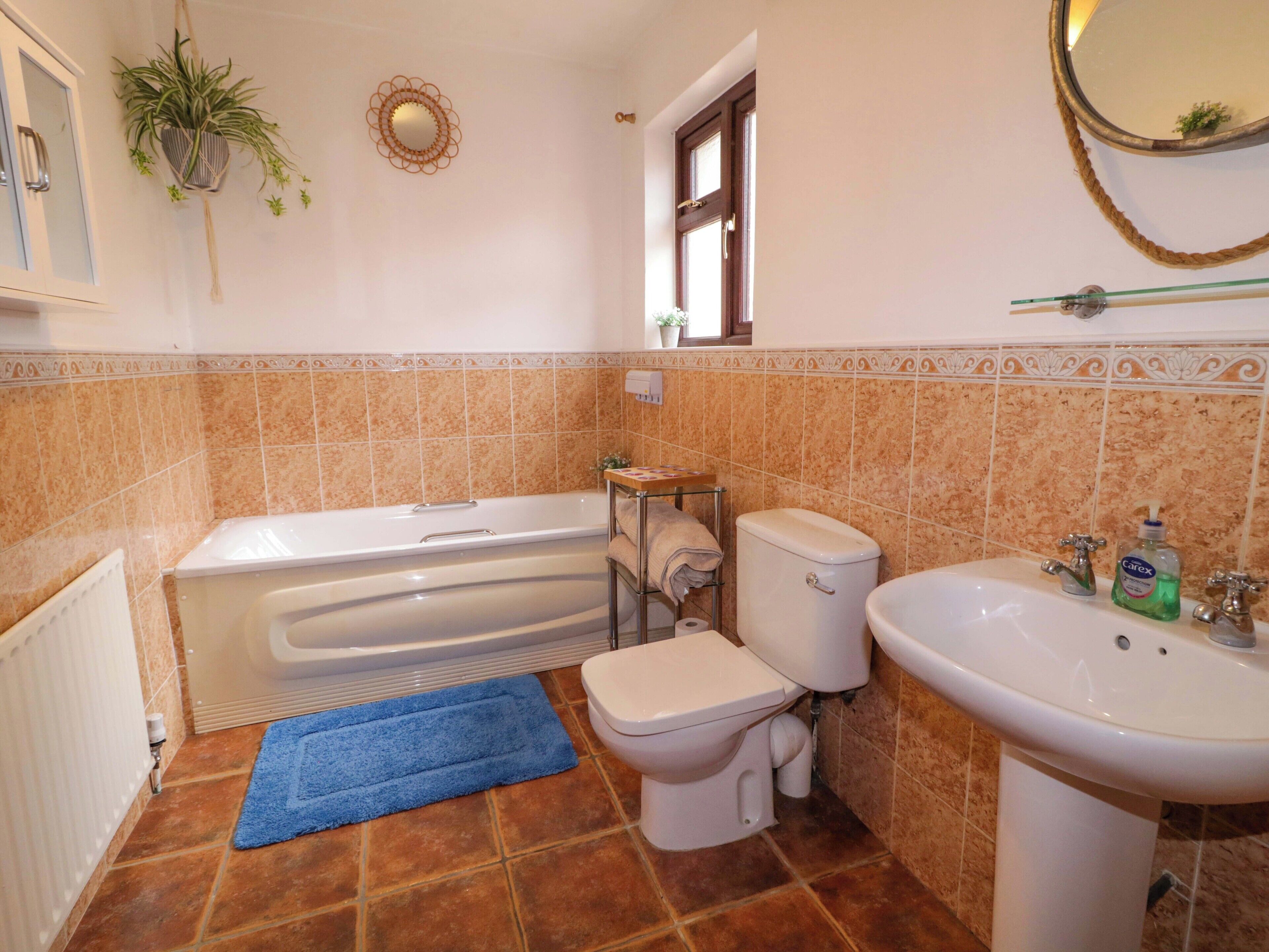 Een badkamer met bad, toilet en wastafel, met bruine tegels en een blauwe badmat.