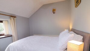 Un dormitori amb un llit, una làmpada de nit, una finestra amb cortines i un quadre petit a la paret.