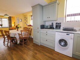 A compact kitchen with a Bosch washing machine, wooden chairs around a table, and a dining area with a window.