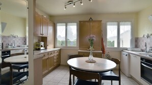 A kitchen with a round dining table, wooden cabinets, and a vase with flowers. - Ker Diskuizh - Proche Sentier G34 (Pléneuf-Val-André)