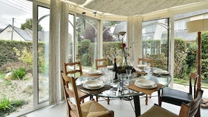 A glass-enclosed dining area with a table set for six, surrounded by wooden chairs. - Ker Diskuizh - Proche Sentier G34 (Pléneuf-Val-André)