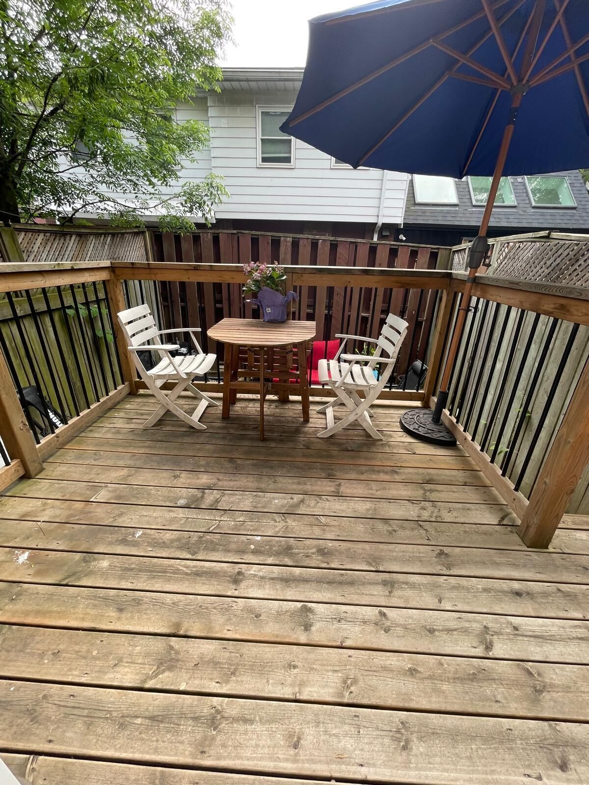 A wooden deck with a table and chairs, a potted plant, and a blue umbrella.