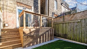 A wooden staircase leading to a glass door, a wooden deck, and a fenced backyard with artificial grass. - 
World Cup Toronto Stay | Stylish 2BR in Roncesvalles/Easy Transit BMO/Yard/BBQ (Toronto)