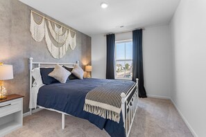 A bedroom with a bed, nightstands, a view through a window, and wall decor. - Modern Country Escape - 5 Min to NIU (Malta)