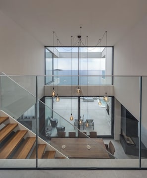A modern interior with a staircase leading to a balcony overlooking the sea.