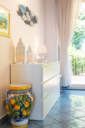 A room with a white cabinet, decorative wall art, a vase with a lemon pattern, and a balcony with a white railing. - CefalHome - Magarà (Sicilia)