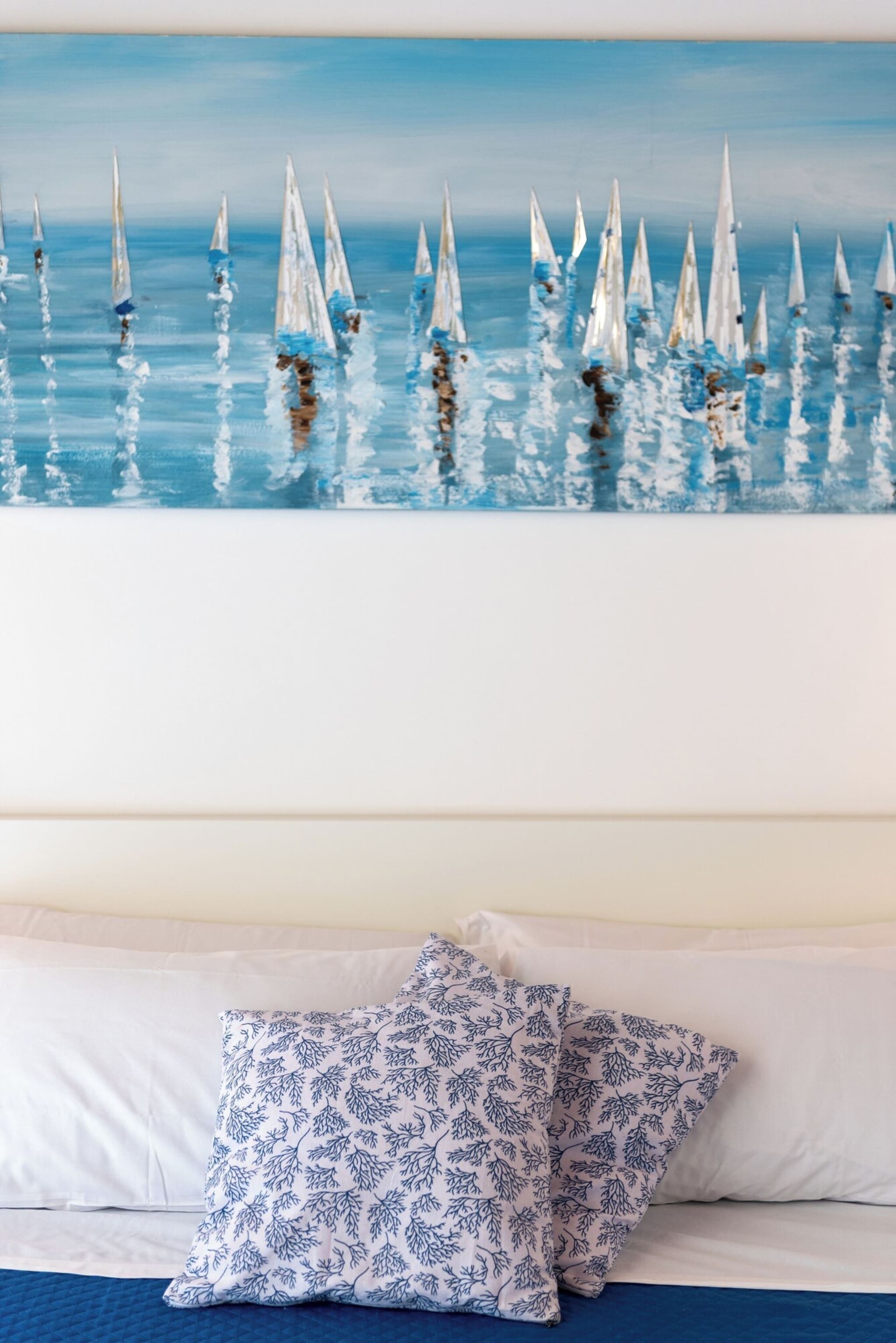 Une chambre à coucher avec un lit, des oreillers et un tableau mural représentant des voiliers sur l’eau.