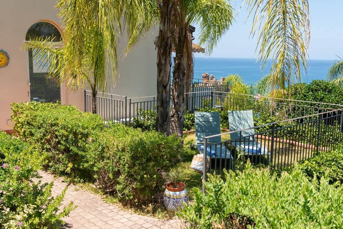 A garden with a pathway, palm trees, and a view of the sea.
