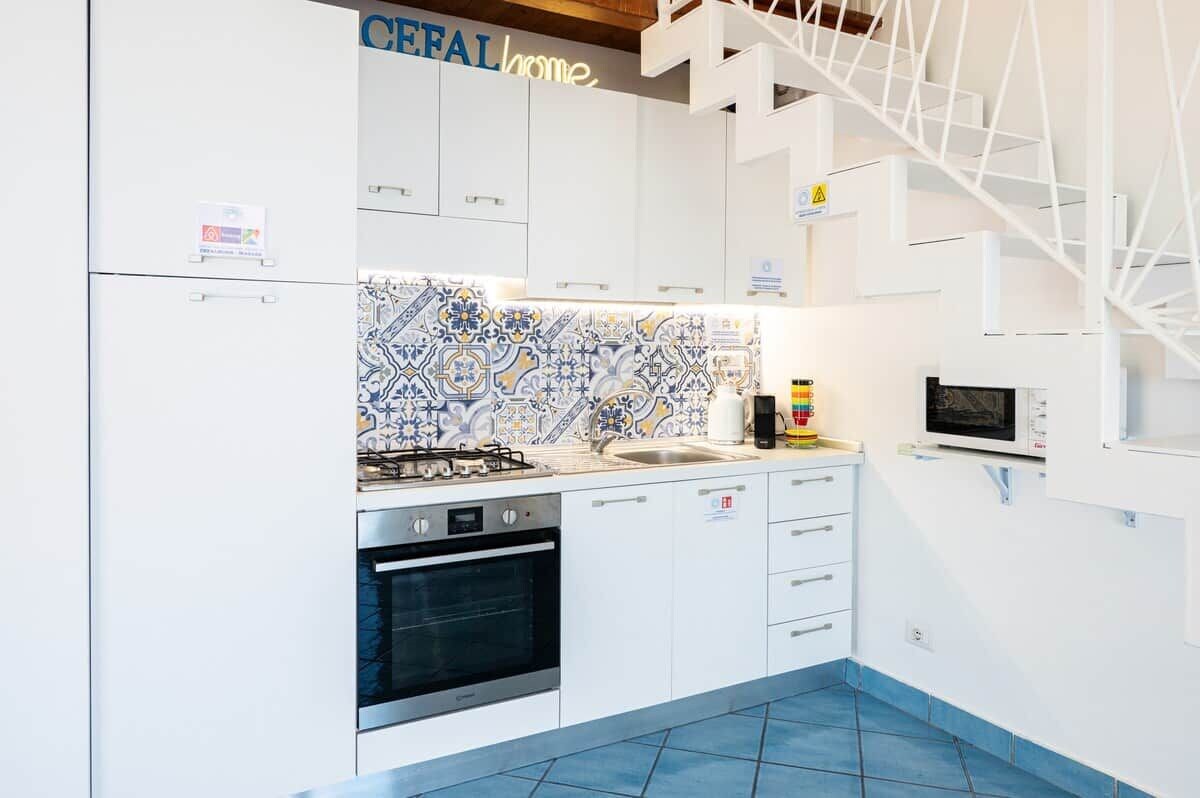 Une cuisine moderne avec des meubles blancs, un crédence à motifs, une cuisinière à gaz, un four et un four à micro-ondes.